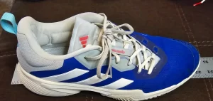 Royal blue and white Adidas Barricade laying atop a metal yardstick to measure length
